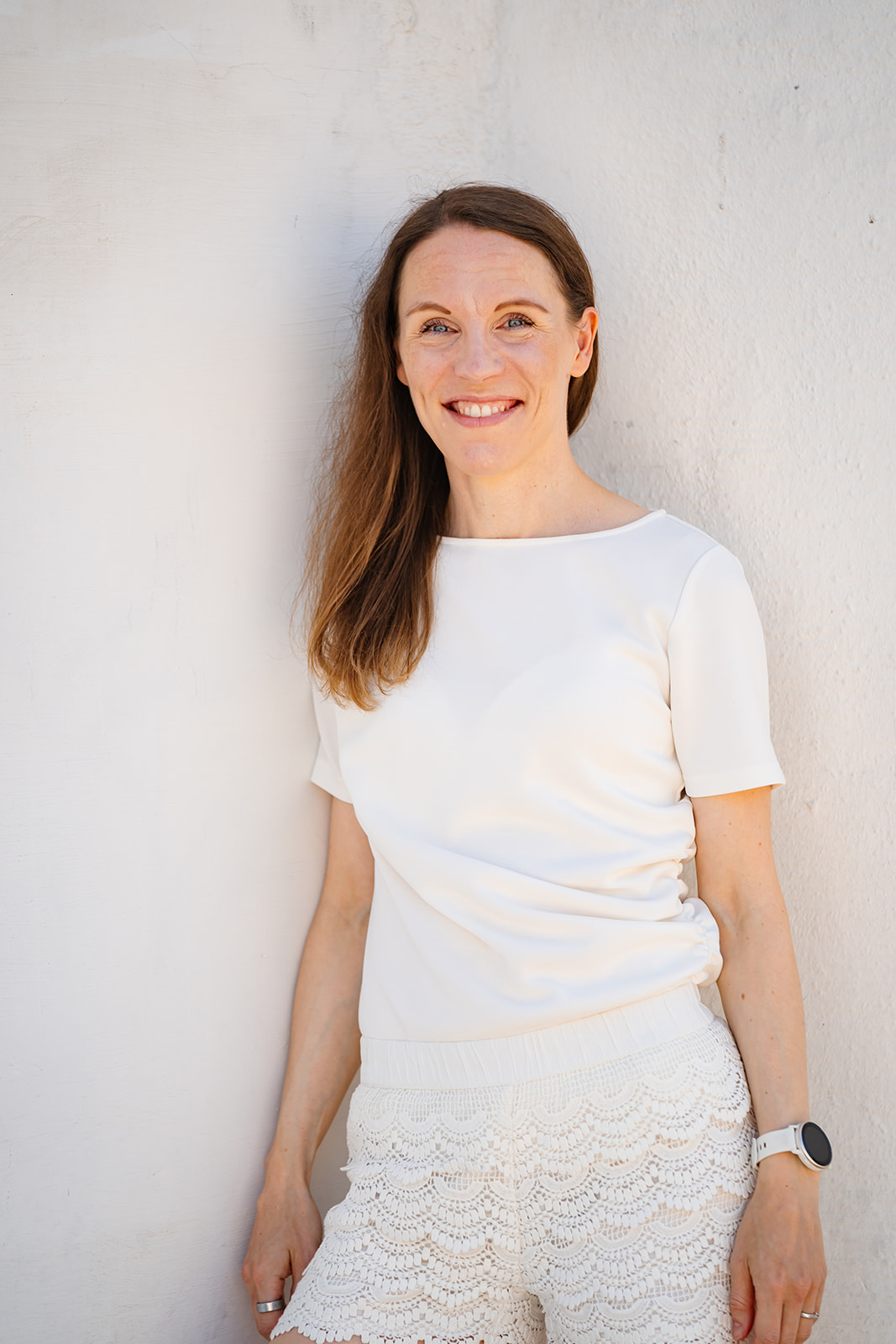 Portrait of Sonja Rajala leaning against a white wall in the sunshine